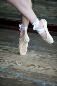 Close-up shot of female feet in ballet shoes dancing on the wooden floor